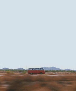 Une camionnette rouge d'époque roule le long d'un paysage désertique avec des montagnes en arrière-plan sous un vaste ciel bleu clair. La scène capture un sentiment de solitude et d'aventure.